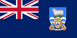 The flag of the Falkland Islands is blue with the UK flag in the canton and the national coat of arms centered in the fly half. The coat of arms has a white ram above a ship, with a scroll at the bottom bearing the motto "DESIRE THE RIGHT."