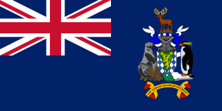 The flag of South Georgia is blue with the UK flag in the canton. The national coat of arms is centered on the fly half and has a green shield with a golden lion holding a torch. A fur seal is to the left of the shield and a Macaroni penguin to the right. A reindeer appears above the crest, and below the shield on a scroll is the Latin motto "LEO TERRAM PROPRIAM PROTEGAT" (Let the Lion Protect its Own Land).